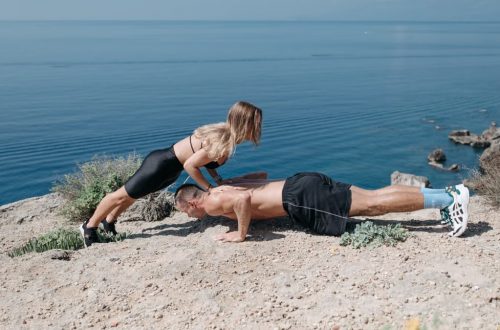 A man and woman perform outdoor fitness exercises on a cliff with a breathtaking sea view.
